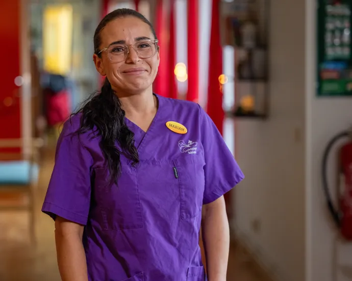 En kvinna i lila operationskläder står i en korridor.