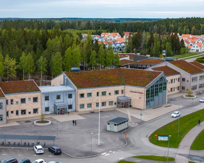 En flygbild av en skolbyggnad med en parkeringsplats framför sig.