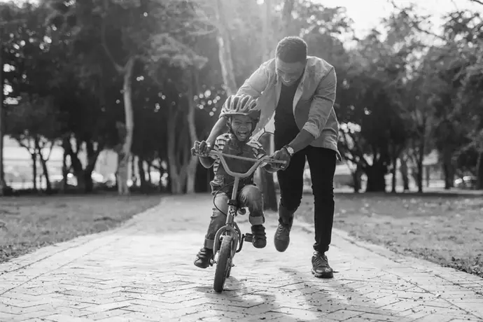 Barn som  cyklar och förälder håller i cykeln. 